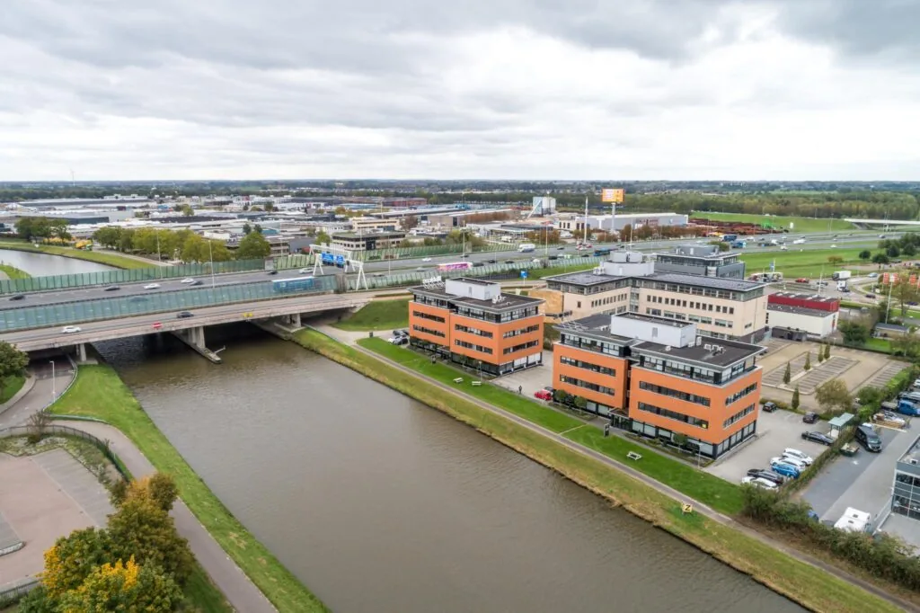 Luchtfoto van kantoorpanden aan de Lage Biezenweg langs een kanaal, met snelwegen en bedrijventerrein op de achtergrond.
